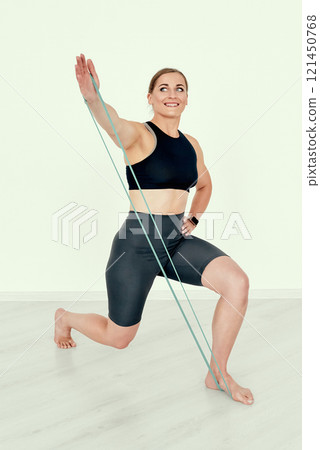 Female Trainer Performing Lunge with Resistance Band and Smile. 121450768