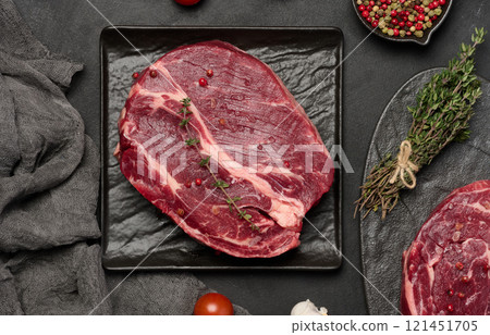 Raw chuck eye roll beef steak on black board, peppercorns, and sprigs of thyme, viewe from above Raw chuck eye roll beef steak on black board, peppercorns, and sprigs of thyme, viewe from above 121451705