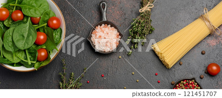 Bunch of spaghetti, plate with green spinach leaves and red chpurri tomatoes on table, top view 121451707