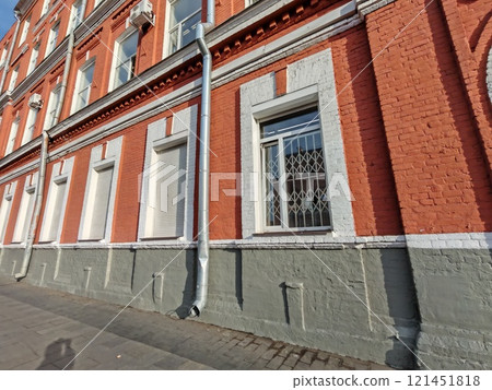 A sturdy metal downspout attached to a textured red brick facade with white window trims. The photo captures construction materials and the importance of drainage systems in urban building 121451818