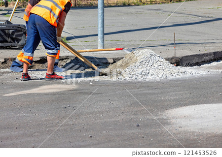 Construction worker repairs a road with gravel and tools in bright sunlight. Copy space. 121453526