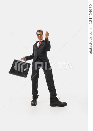 Man wearing black suit and glasses energetically dancing with briefcase, creating humorous and lively expression against white studio background. 121454670
