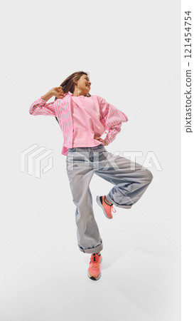 Woman energetically dancing in pink and denim outfit, radiating joy and confidence against white studio background. 121454754