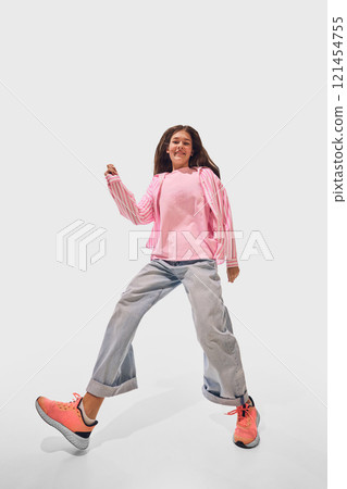 Wide angle photo of woman in pink striped shirt and loose denim playfully dancing expressing movement and balance against white studio background. Wide angle photo of woman in pink striped shirt and loose denim playfully dancing expressing movement and balance against white studio background. 121454755