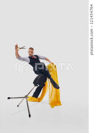 Man dynamically wraps yellow fabric around black mannequin, holding scissors with precision against white studio background. Man dynamically wraps yellow fabric around black mannequin, holding scissors with precision against white studio background. 121454764