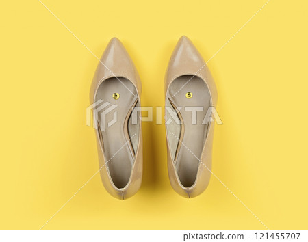Pair of beige classic women's shoes with pushpin on yellow background. Pranks and tricks concept for April fool's day with copy space 121455707