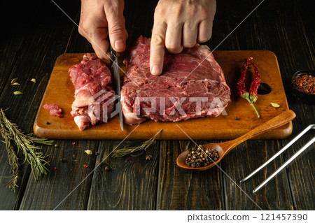 A skilled chef expertly slices raw meat on a wooden cutting board, surrounded by fresh herbs and spices. The warm, inviting atmosphere evokes a love for cooking and culinary craftsmanship A skilled chef expertly slices raw meat on a wooden cutting board, surrounded by fresh herbs and spices. The warm, inviting atmosphere evokes a love for cooking and culinary craftsmanship 121457390