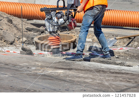 Construction worker operates machinery on urban street during daylight hours. Copy space. 121457828