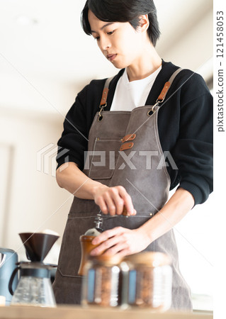 一位年輕的男咖啡師仔細研磨咖啡豆 一位年輕的男咖啡師仔細研磨咖啡豆 121458053