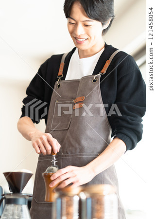 一位年輕的男咖啡師仔細研磨咖啡豆 一位年輕的男咖啡師仔細研磨咖啡豆 121458054