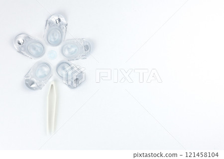 Top view of a creative flower consisting of containers for daily contact lenses, in the center there is a soft bluish lens, down like the stem of a plant there are tweezers for taking lenses on a 121458104