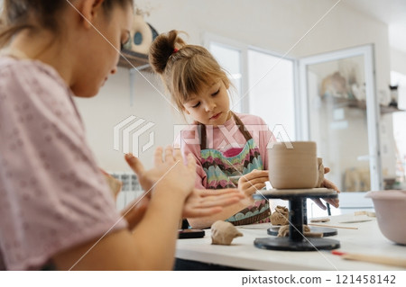 Creating pottery together in a cozy studio by a child and an adult Creating pottery together in a cozy studio by a child and an adult 121458142