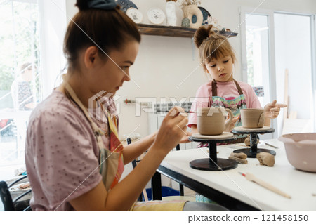 Creative pottery session between a mother and daughter in a bright studio Creative pottery session between a mother and daughter in a bright studio 121458150