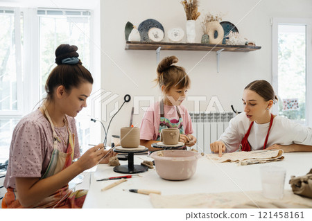 Women and child engaged in pottery at a cozy studio during the day Women and child engaged in pottery at a cozy studio during the day 121458161