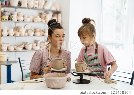 A pottery class where an adult teaches a child to shape clay in a studio 121458164