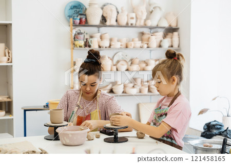 A mother and daughter create pottery together in a sunny art studio A mother and daughter create pottery together in a sunny art studio 121458165