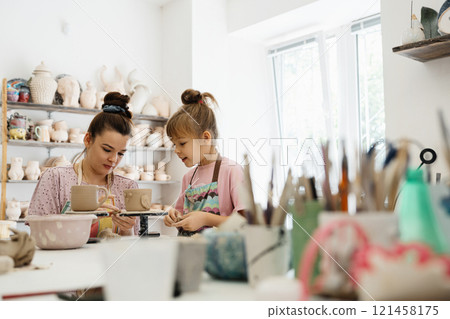 A mother and daughter enjoy pottery making together in a bright studio A mother and daughter enjoy pottery making together in a bright studio 121458175