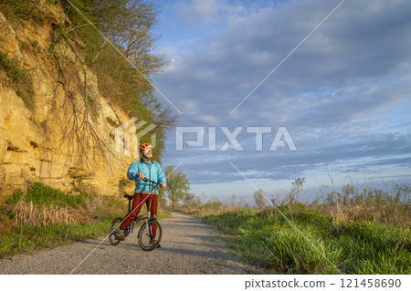 senior male cyclist riding a folding bike on Steamboat Trace, bike trail converted from an abandoned railroad, near Peru, Nebraska, springtime morning scenery 121458690