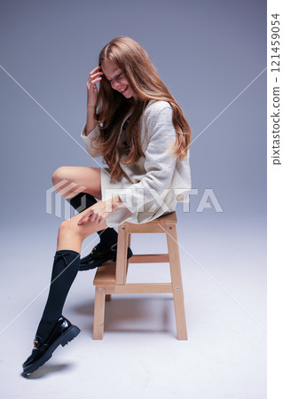 A Stylish Young Woman is Comfortably Sitting on a Stool, exuding confidence and charm 121459054