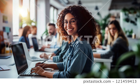 Young woman smiling while working on laptop in a bright office environment during the afternoon 121459413