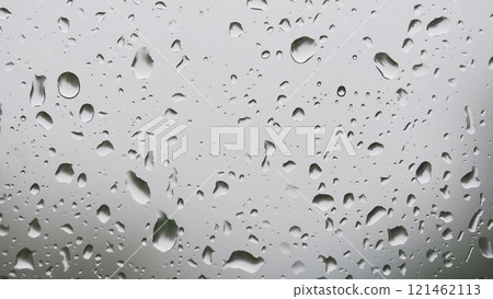 Rain Droplets on Glass - Close-up view of raindrops scattered across a glass surface. The background is softly blurred with a grayish tone, emphasizing the shapes and clarity of the water droplets. 121462113