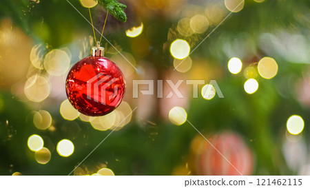a red Christmas ornament hanging delicately from a tree branch. The background is beautifully blurred, showcasing golden bokeh lights, giving it a warm and festive feel. The reflection on the ornament 121462115