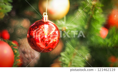 a vivid red Christmas ornament hanging amidst lush green branches. The soft bokeh effect in the background adds depth and warmth, creating a cheerful and festive holiday vibe a vivid red Christmas ornament hanging amidst lush green branches. The soft bokeh effect in the background adds depth and warmth, creating a cheerful and festive holiday vibe 121462119
