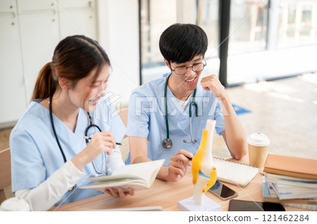 A female medical student is examining a model of bone joints and discussing it with her classmate. 121462284