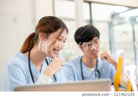 A female medical student is examining a model of bone joints and discussing it with her classmate. 121462285