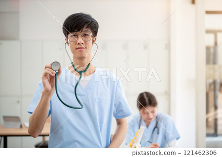 A smart Asian male medical student in scrubs, smiling and showing his stethoscope to the camera. 121462306