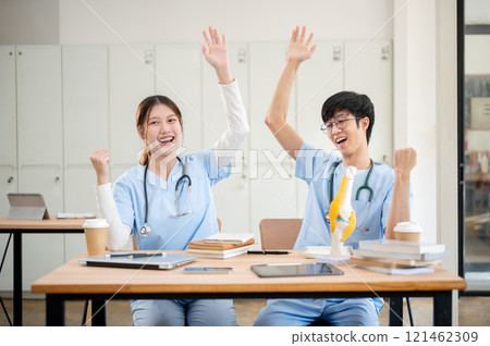 Two cheerful medical students in scrubs are raising their hands to celebrate their achievement. Two cheerful medical students in scrubs are raising their hands to celebrate their achievement. 121462309