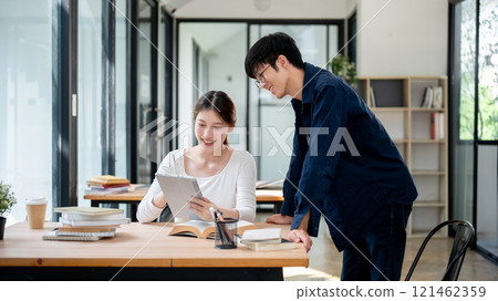 Two positive Asian college students are looking at a tablet screen and discussing. 121462359