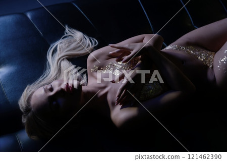 Elegant figure lounging on a dark couch adorned in gold accents at night Elegant figure lounging on a dark couch adorned in gold accents at night 121462390
