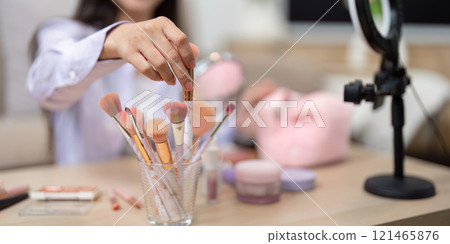 Asian woman selecting makeup brush from collection on table Asian woman selecting makeup brush from collection on table 121465876