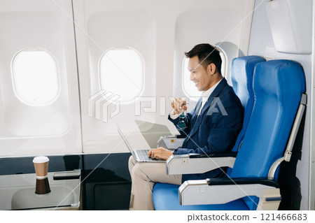 Attractive Asian male passenger of airplane sitting in comfortable seat while working laptop and tablet with mock up area using wireless connection. Attractive Asian male passenger of airplane sitting in comfortable seat while working laptop and tablet with mock up area using wireless connection. 121466683