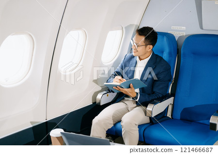 Attractive Asian male passenger of airplane sitting in comfortable seat while working laptop and tablet with mock up area using wireless connection. 121466687