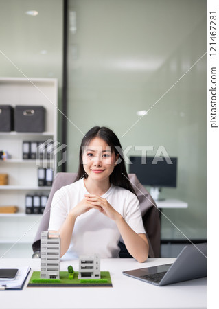 Young real estate agent worker working with laptop and tablet at table in office and small house beside it. 121467281