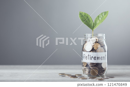 Glass jar filled with coins and a sprout labeled 'Retirement,' placed on a table with a gray background, symbolizing saving for financial growth and secure future planning 121470849