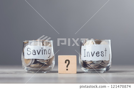 Concept of choosing between saving money or investing, illustrated by two glass jars filled with coins, one labeled "Saving" and the other "Invest," Decision-making process for financial growth Concept of choosing between saving money or investing, illustrated by two glass jars filled with coins, one labeled "Saving" and the other "Invest," Decision-making process for financial growth 121470874