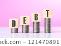 Stack of coins neatly arranged on top of a wooden block labeled "DEBT," symbolizing financial burdens and the weight of monetary obligations, set against a neutral background to emphasize the concept 121470891