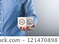 A man holds a wooden block with a smiling face, symbolizing positivity and happiness. This image reflects the concept of embracing joy and maintaining an optimistic outlook 121470898