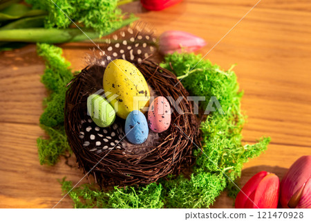 Easter colored eggs in a nest feathers moss tulips on a wooden board Easter colored eggs in a nest feathers moss tulips on a wooden board 121470928