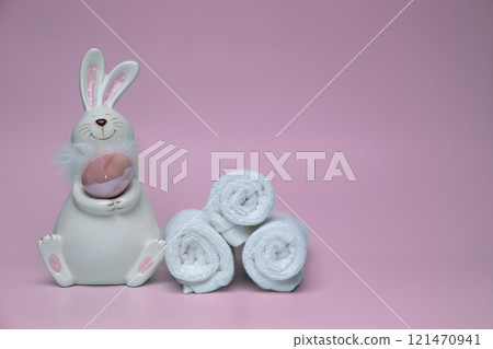 Sculpture of white rabbit with Easter eggs on pink background with white towels Sculpture of white rabbit with Easter eggs on pink background with white towels 121470941