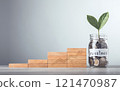 Glass jar filled with coins and a sprout labeled "Investment," placed beside stacked wooden blocks arranged like stairs with interest symbols, symbolizes financial growth, incremental savings 121470987