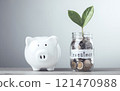 Glass jar filled with coins and a sprout labeled "Investment," placed next to a white piggy bank, Saving and investing for the future. Financial growth, long-term planning management strategies. 121470988