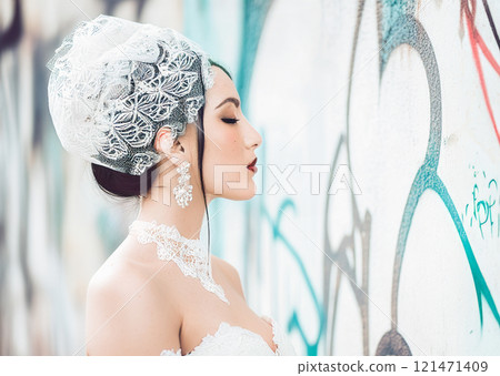 The image features a woman dressed in a vintage-style bridal look,complete with a white lacy corset and a decorative headpiece,set against a gritty, urban background 121471409