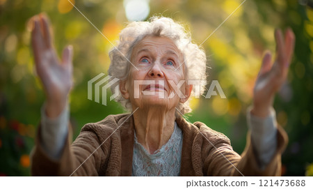 Elderly woman with arms raised, looking upwards. 121473688
