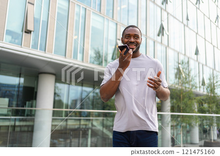 African american man talking on smartphone on street in city outdoor. Man with cell phone chatting with friends. Smiling person making answering call by cellphone. Guy having conversation by mobile African american man talking on smartphone on street in city outdoor. Man with cell phone chatting with friends. Smiling person making answering call by cellphone. Guy having conversation by mobile 121475160