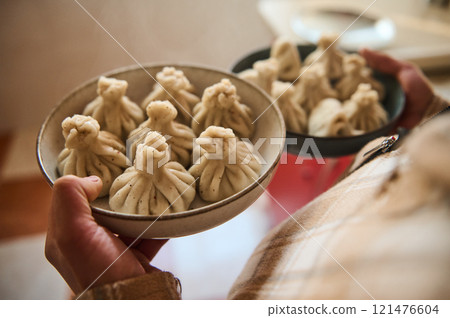 Hand holding plates of homemade Georgian dumplings in a kitchen setting 121476604