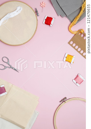Beige cotton cloth in embroidery hoop with fabric, colorful threads, scissors and needls. Embroidery set fot stitching 121476635